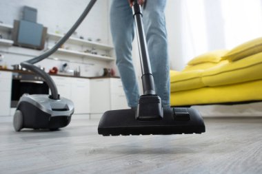 Evdeki bulanık arka planda, insanın yakınındaki elektrikli süpürgenin kırpılmış görüntüsü 