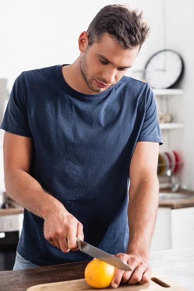 Young Man Cutting Fresh Orange Cutting Board Blurred Foreground — Stock Photo, Image