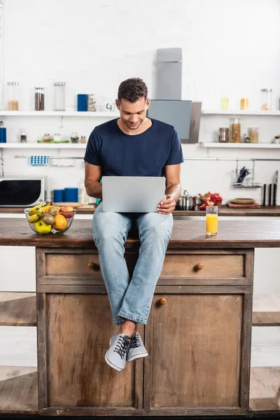 Jovem Usando Laptop Perto Suco Laranja Frutas Mesa Cozinha — Fotografia de Stock