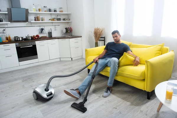 Young Man Holding Vacuum Cleaner While Sitting Couch Home — Stock fotografie