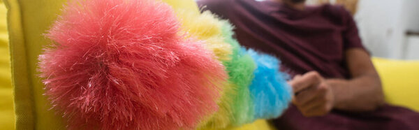 Обрезанный вид пыли кисти в руке человека на размытом фоне на диване, размытый 