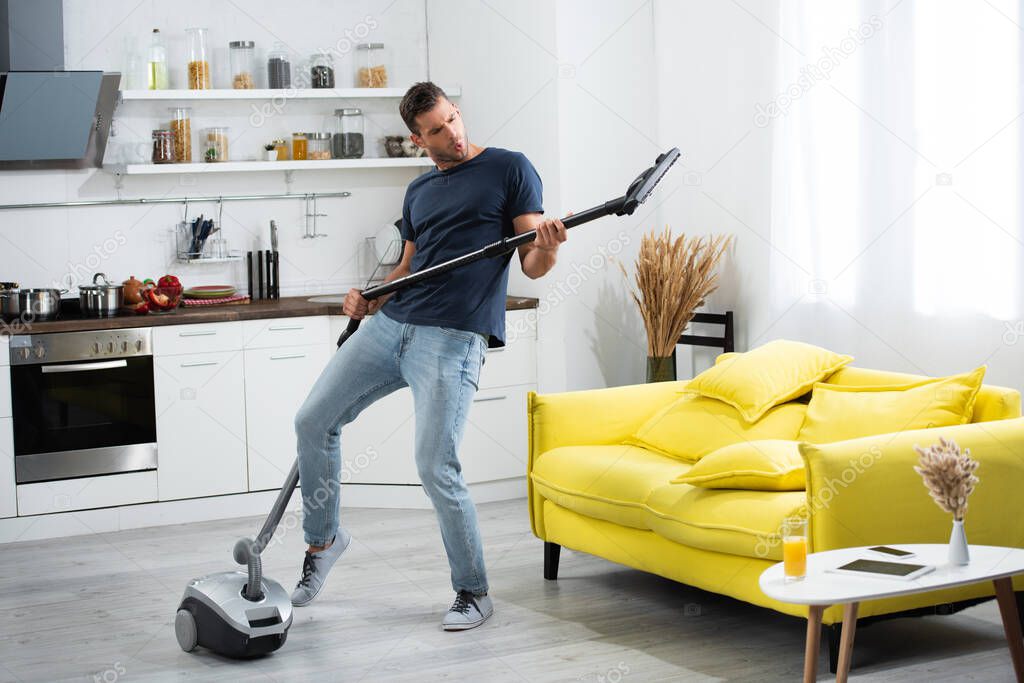 Excited man having fun while holding brush of vacuum cleaner at home 