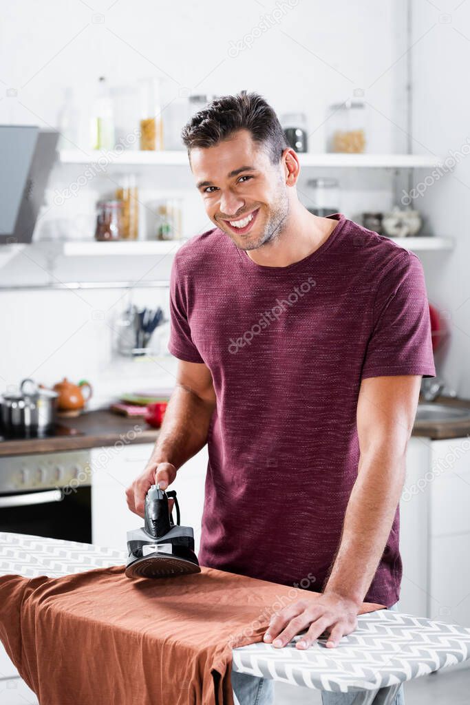 Smiling man holding iron near clothes on board at home 