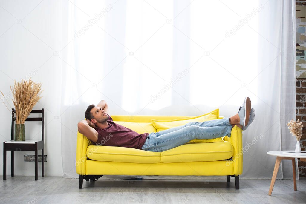 Smiling man with hands near head lying on couch at home 