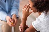 Közelkép afro-amerikai lány kéz a szemben sírás során konzultáció elmosódott pszichológus a háttérben