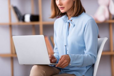 Cropped view of female psychologist using laptop while sitting on chair on blurred background clipart