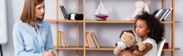 Female Psychologist Looking Upset African American Girl Hugging Teddy Bear — Stock Photo, Image