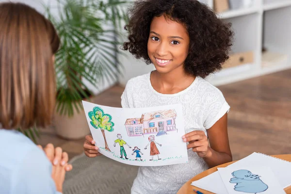 Cheerful African American Girl Showing Drawing Family Blurred Psychologist Foreground — Stock Photo, Image