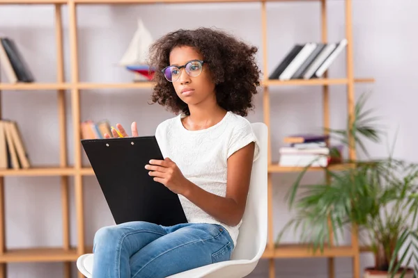 African American Girl Eyeglasses Clipboard Looking Away While Sitting Chair — Stock Photo, Image