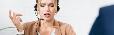 Serious female consultant in headset gesturing on blurred foreground, banner clipart