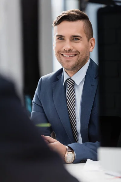 Glad Affärsman Sitter Arbetsplatsen Med Suddig Medarbetare Förgrunden — Stockfoto