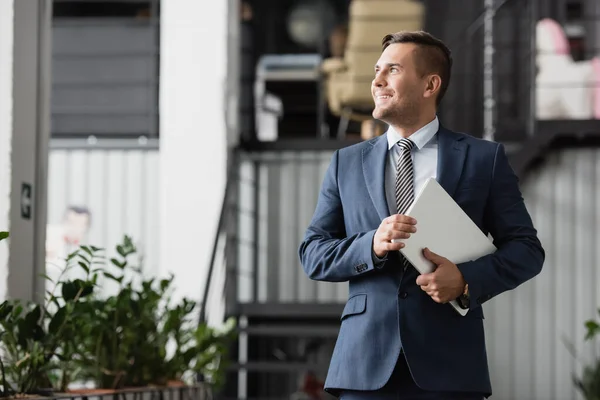 Smiling Businessman Laptop Looking Away While Standing Work Blurred Background — Stock Photo, Image