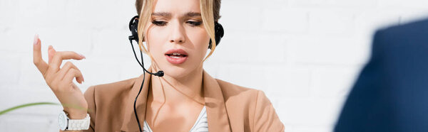 Serious female consultant in headset gesturing on blurred foreground, banner