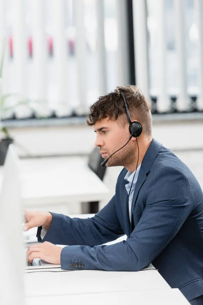 Oldalsó Nézet Súlyos Operátor Headset Gépelés Laptop Miközben Asztalnál Homályos — Stock Fotó