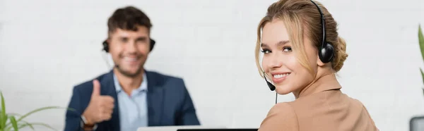 Sonriente Operador Femenino Auriculares Mirando Cámara Con Compañero Borroso Fondo — Foto de Stock