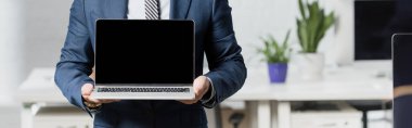 Resmi giyimde yöneticinin görüntüsü, arka planda bulanık ofis, pankart ve boş ekran ile dizüstü bilgisayarı gösteriyor