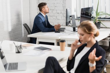 İş yerinde odaklanmış bir iş adamı bulanık bir meslektaşla ön planda telefonla konuşuyor.
