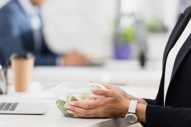 Plastik kâse tutan kadın yöneticinin iş yerinde yediği bulanık arka plan görüntüsü.