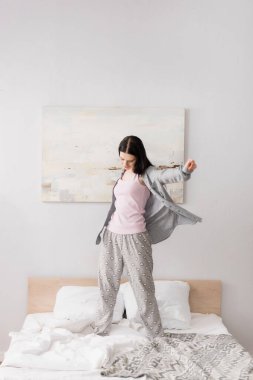 full length of happy woman with vitiligo stretching while standing on bed clipart