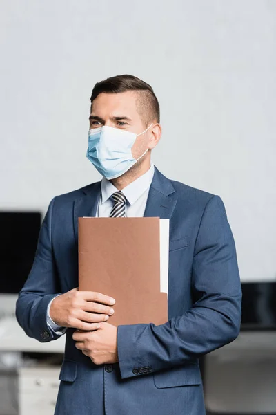 Επιχειρηματίας Ιατρική Μάσκα Φάκελο Κοιτάζοντας Μακριά Ενώ Στέκεται Στο Γραφείο — Φωτογραφία Αρχείου