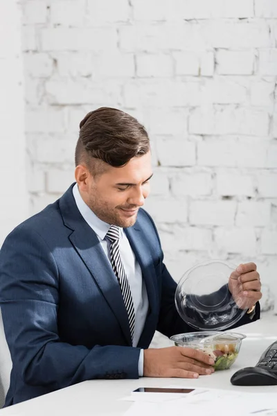 Hombre Negocios Sonriente Abriendo Tazón Plástico Con Comida Mientras Está — Foto de Stock