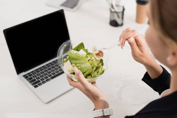 High angle view of businesswoman holding plastic fork and meal in bowl at workplace on blurred foreground
