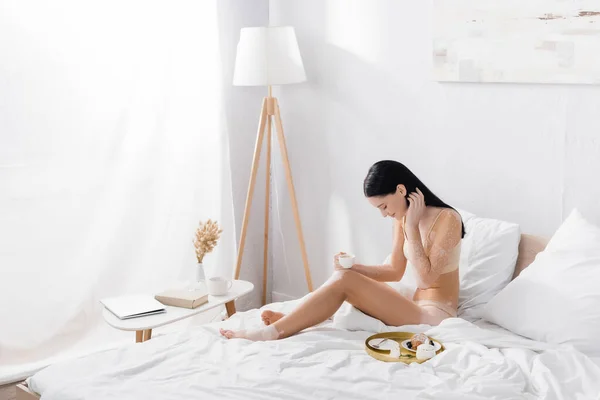 年轻女子与白垩风杯靠近早餐托盘在床上 — 图库照片