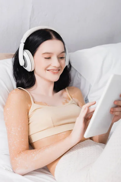 寝室でデジタルタブレットを保持している無線ヘッドフォンで白斑と幸せな若い女性 — ストック写真
