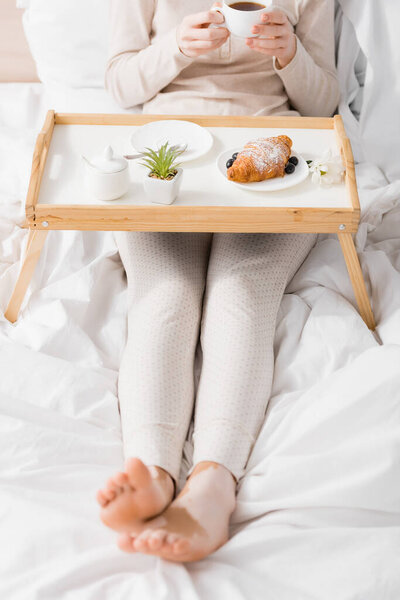 cropped view of woman with vitiligo holding cup near breakfast on tray
