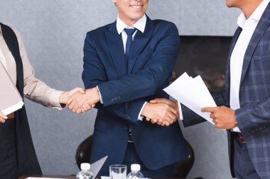 Cropped view of businessman shaking hands with multicultural colleagues in meeting room clipart