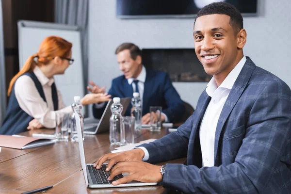 Empresário Afro Americano Feliz Olhando Para Câmera Enquanto Digita Laptop — Fotografia de Stock