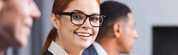 Happy Redhead Businesswoman Eyeglasses Looking Camera Blurred African American Man — Stock Photo, Image