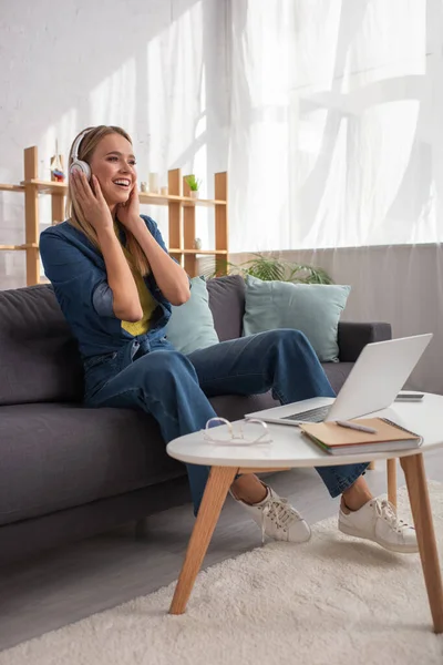 Penuh Panjang Wanita Pirang Ceria Headphone Tertawa Sambil Duduk Sofa — Stok Foto