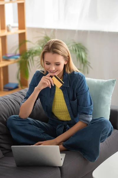 Sonriente Joven Rubia Con Tarjeta Crédito Mirando Computadora Portátil Mientras —  Fotos de Stock