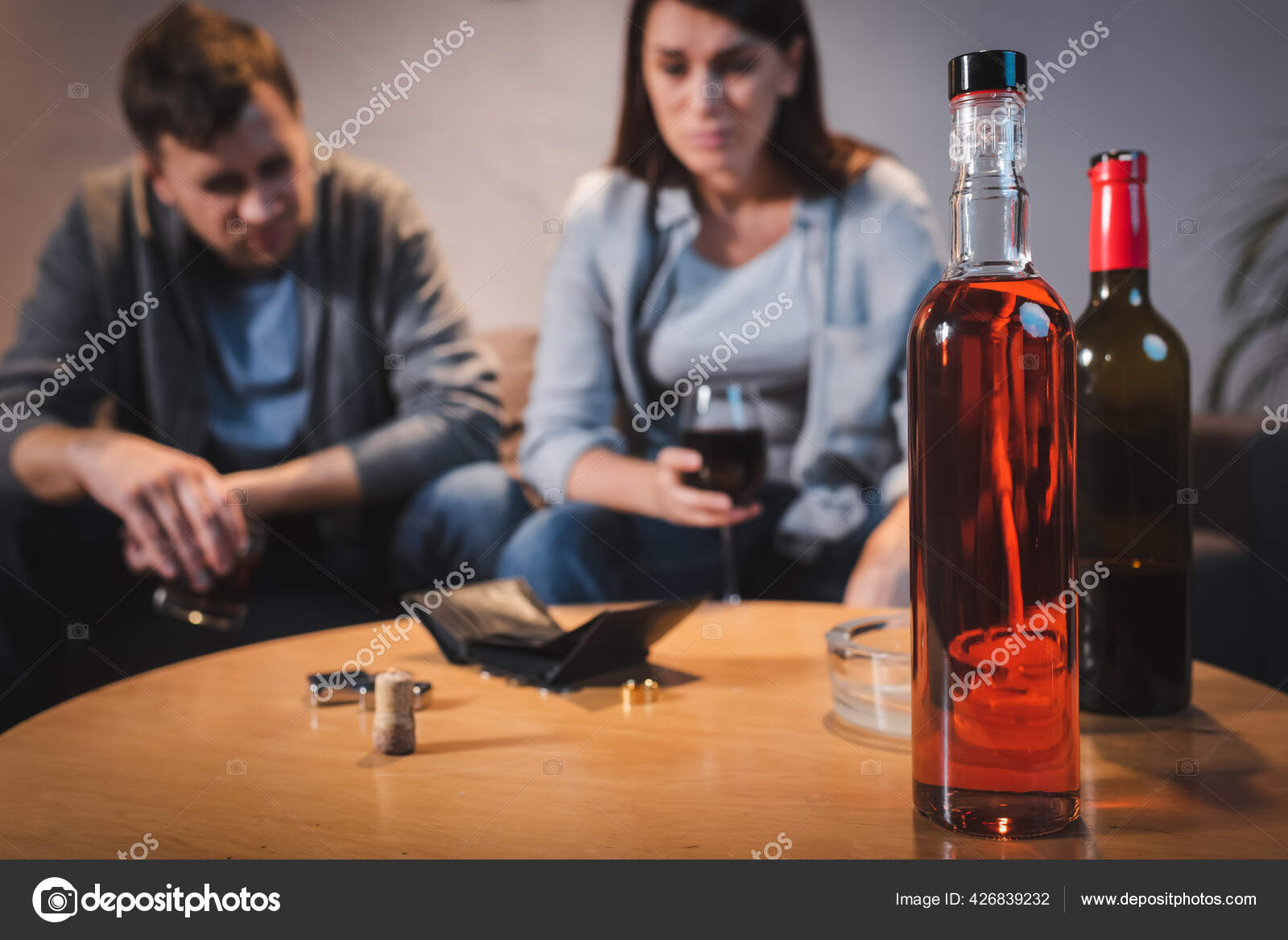 酒瓶和空皮夹在醉汉夫妇近旁的桌上背景模糊 图库照片 C Andrewlozovyi
