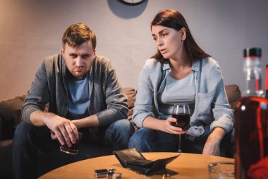 depressed, drunk couple sitting at table with alcohol drinks and empty wallet, blurred foreground clipart