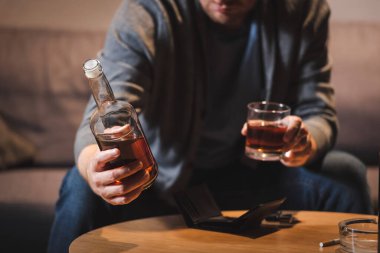 Alkolik bir adamın evde şişe ve bir bardak viski tutarken görüntüsü bulanık.