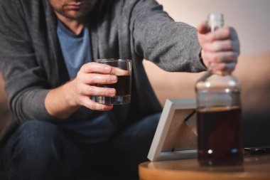 Kırpılmış cam ve viski şişeli sarhoş adam görüntüsü fotoğraf çerçevesinin yanında, bulanık ön plan