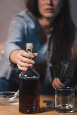 Masadan viski şişesini alan alkolik kadının kısmi görüntüsü, bulanık arka plan