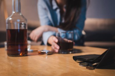 Alkol bağımlısı bir kadının bozuk paralarla cüzdanın yanında viski içmesi, bulanık bir arka plan.