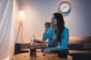 Evde tek başına oturmuş viski içen hayal kırıklığına uğramış bir kadın.
