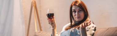 drunk, skeptical woman looking at camera while holding glass of red wine, banner     clipart