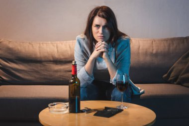 Kızgın alkolik kadın kırmızı şarap, bozuk para ve boş cüzdanla masada oturuyor. 