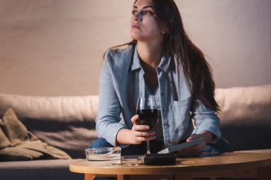 Hayal kırıklığına uğramış, alkol bağımlısı bir kadın fotoğraf çerçevesi ve bir kadeh şarapla otururken başka tarafa bakıyor.    