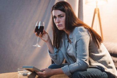 Hüsrana uğramış bir kadın elinde kırmızı şarap kadehi ve fotoğraf çerçevesiyle evde yalnız başına.