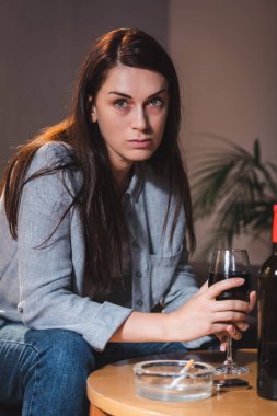 Alkolik kadın kırmızı şarap kadehiyle evde tek başına otururken gözlerini kaçırıyor. 