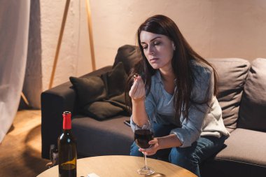 Alkol bağımlısı bir kadın kırmızı şarap kadehiyle otururken elinde alyans tutuyor.