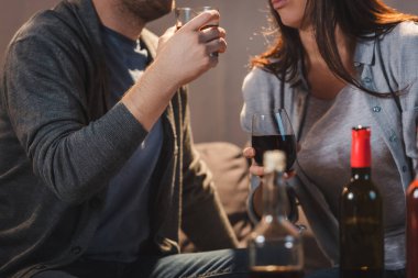 Ön plandaki bulanık şişelerin yanında viski ve şarap içen çiftin görüntüsü.