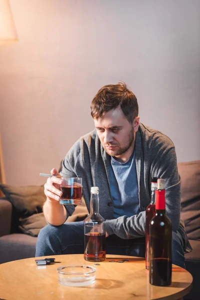 Deprimido Hombre Solitario Sosteniendo Vaso Whisky Cerca Botellas Mesa Casa — Foto de Stock