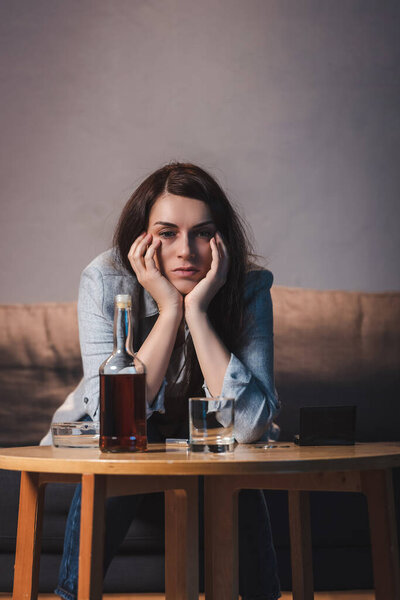 depressed woman sitting near bottle of whiskey at home alone